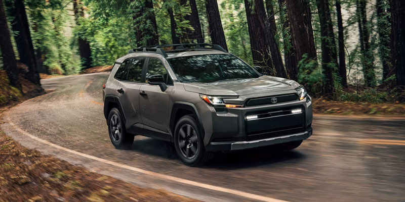Gray Toyota SUV driving on a winding forest road with motion blur through tall trees.
